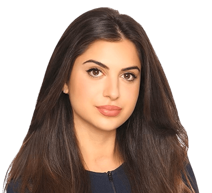 Woman with long brown hair and a neutral expression, wearing a dark top against a plain background.