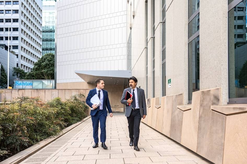 Two people in business attire, possibly family lawyers from Brisbane, walk and converse outside modern office buildings.