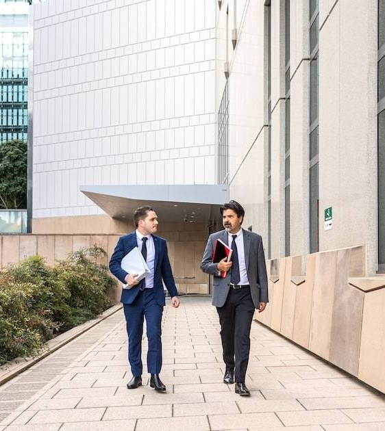 Two businessmen discuss a child support lawyer outside a modern office building.