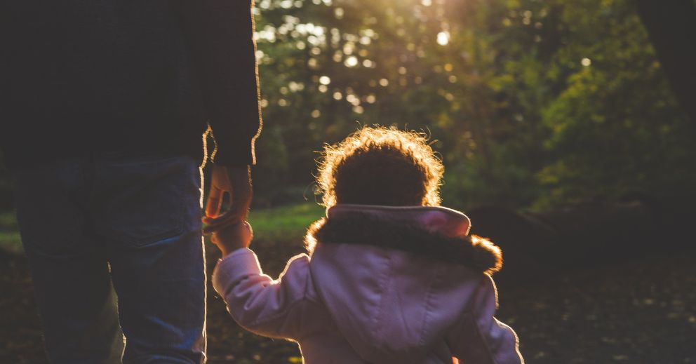 A recently divorced and child holding hands while walking outdoors in sunlight wondering about the what a consent order in family law is