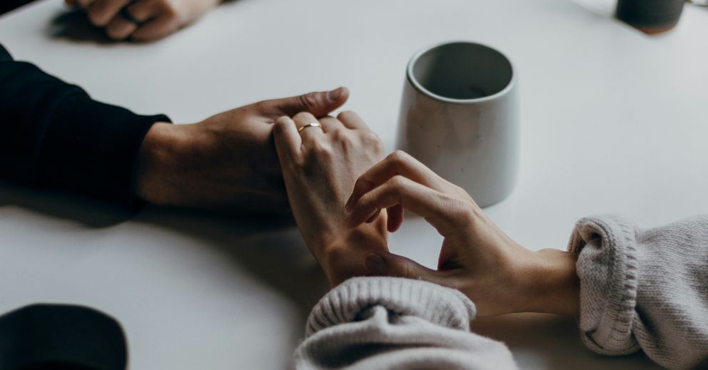 Two people holding hands on a table with a cup nearby discussing divorce