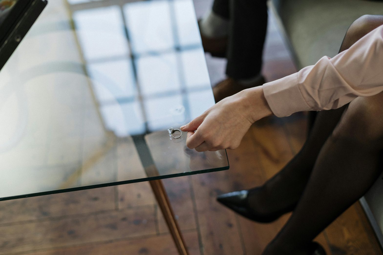 Person placing a ring on a glass table with a wooden floor below.