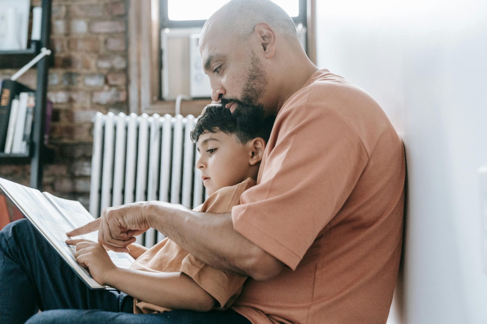 Man reading a book with a child sitting on his lap in a cozy room.