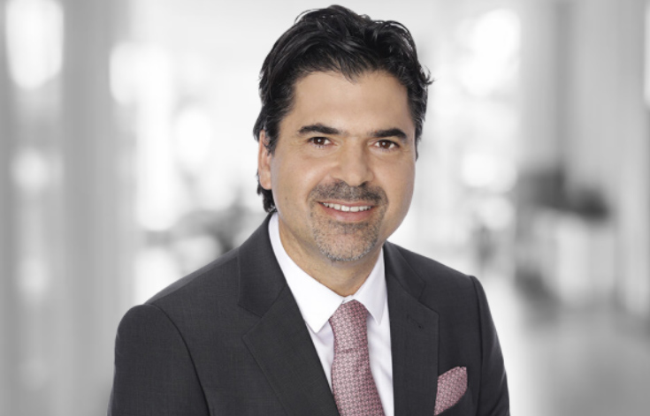 Man in a dark suit, pink tie, and child support lawyer smiling in a blurred office setting.