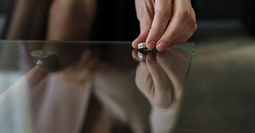 A hand places a ring on a glass table.