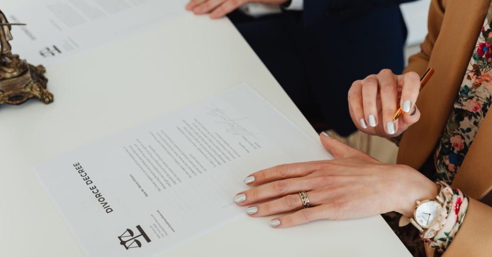 Person signing a divorce decree document at a desk with another individual present and finding out how filing for divorce in Brisbane works
