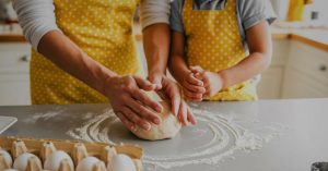 Two people in yellow polka dot aprons, like a parent relocating with a child, knead dough together.