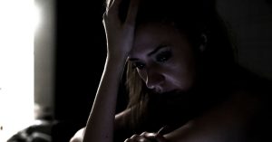 A woman in a dimly lit room, distressed, considers a domestic violence protection order.