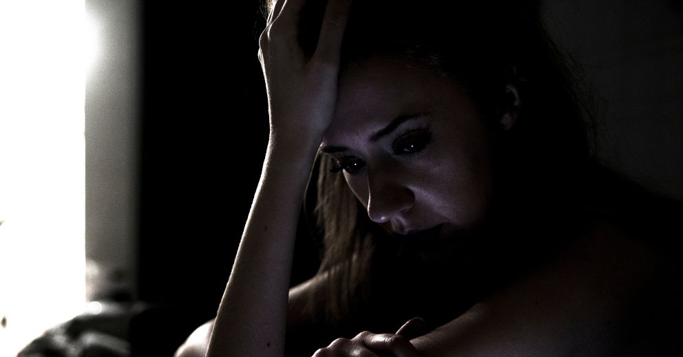 A woman in a dimly lit room, distressed, considers a domestic violence protection order.