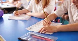 Students in white shirts work at a blue desk amid schooling disputes between separated parents.