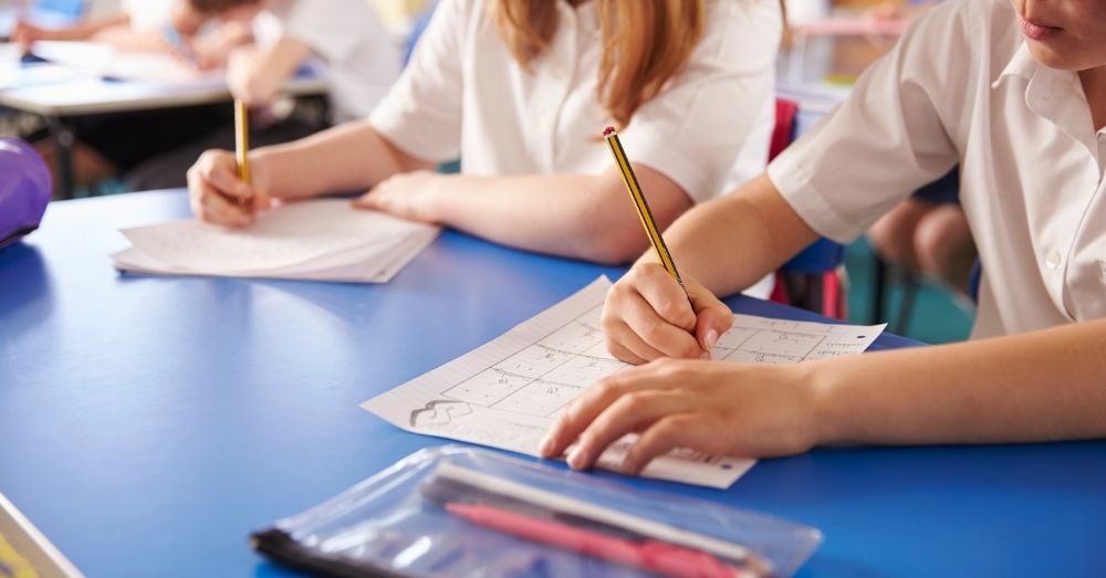 Students in white shirts work at a blue desk amid schooling disputes between separated parents.