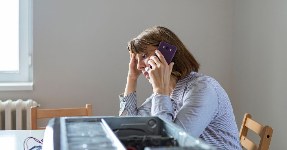 A woman holding a phone looks concerned near an open computer case on a table.